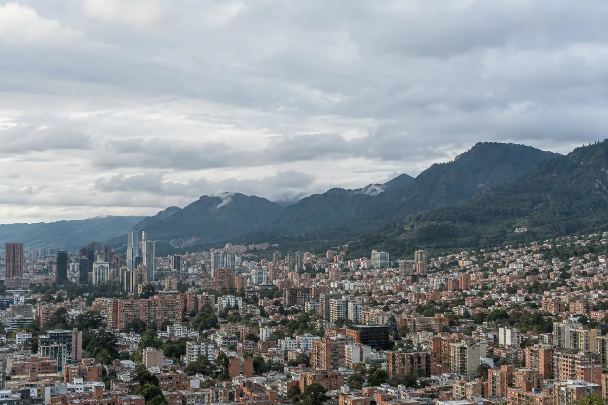 Vista panorámica de Bogotá bajo cielo nublado, con los cerros orientales al fondo y la ciudad de ladrillo extendiéndose en la sabana; Vigomez distribuye fruta importada desde su sede en Corabastos